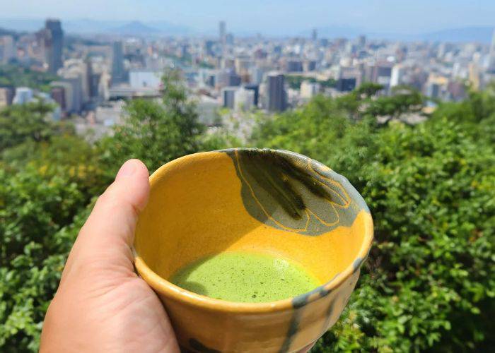 A hand holding a fresh bowl of matcha above the city of Hiroshima.